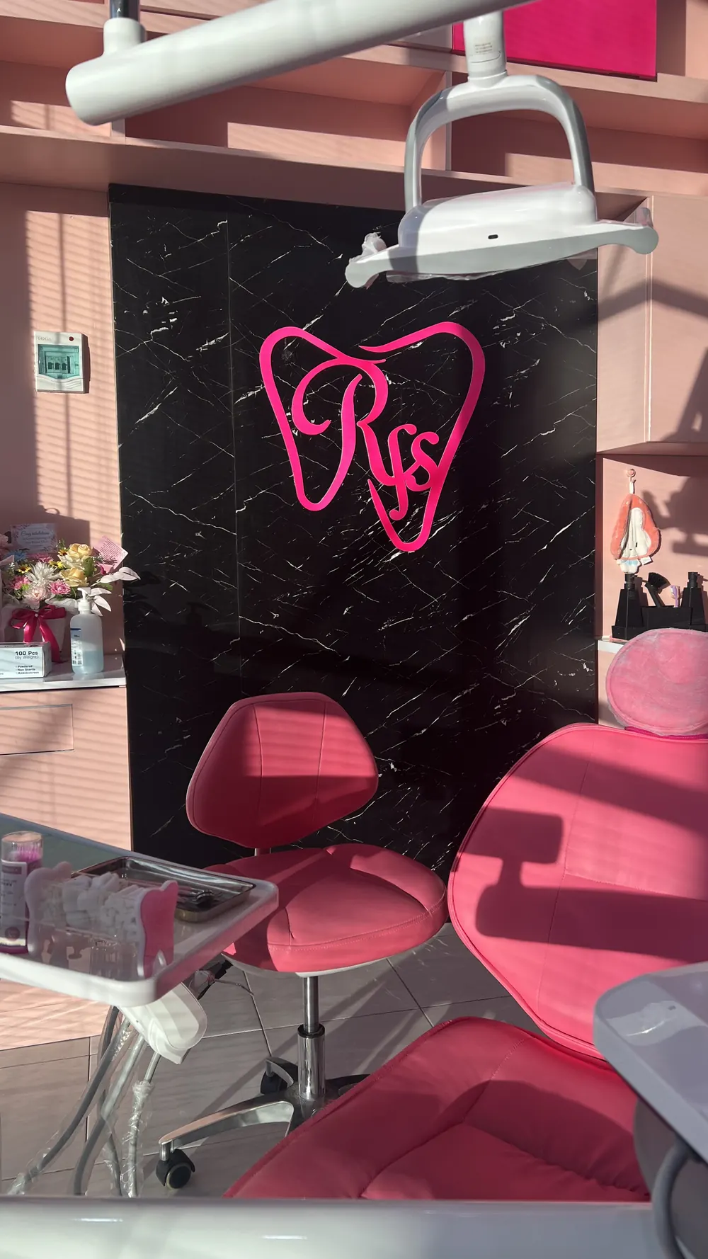 Kursi dental pink di depan dinding marmer hitam berlogo RFS